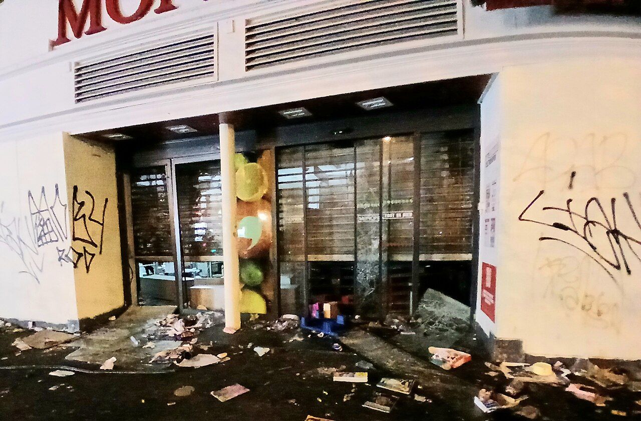 一間遭洗劫的 Monoprix 超市入口,玻璃破碎、地上滿是雜物