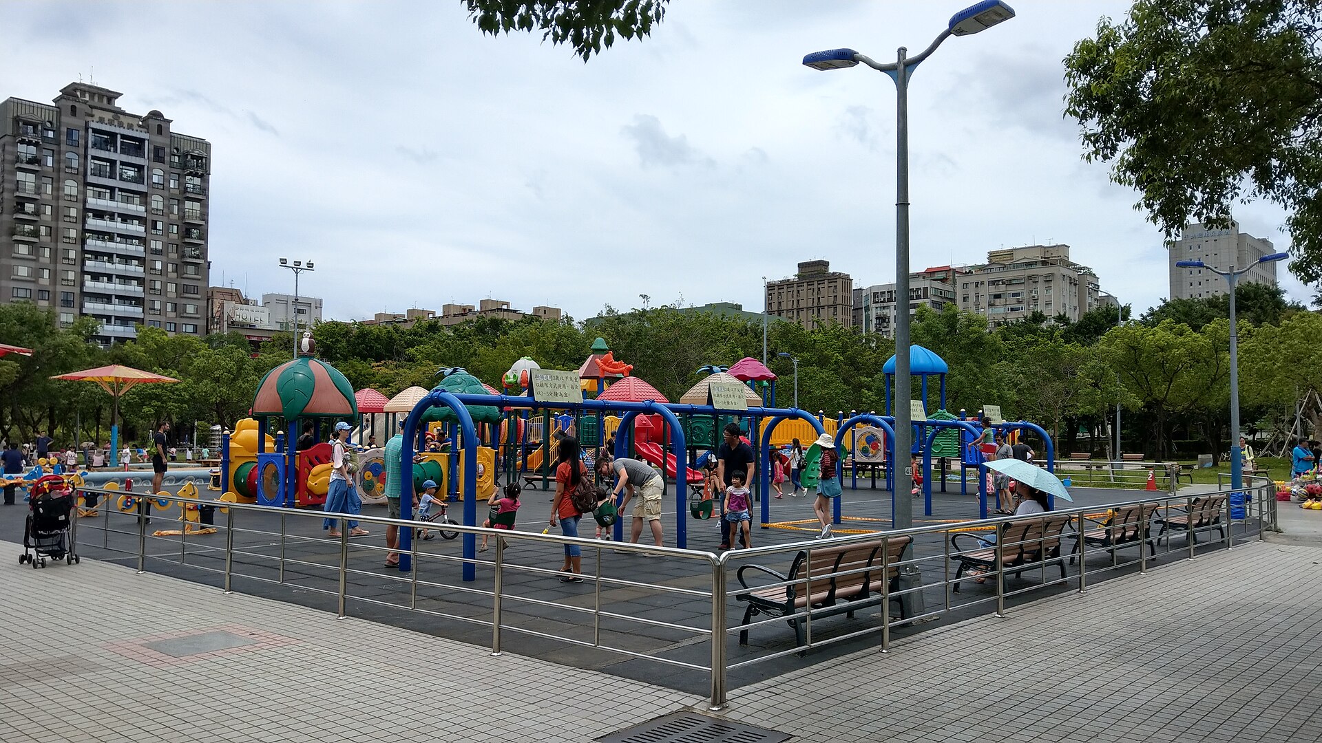 A children’s playground in Taipei’s Daan Forest Park: colourful slides and climbing frames with a few parents and children, apartment blocks behind.